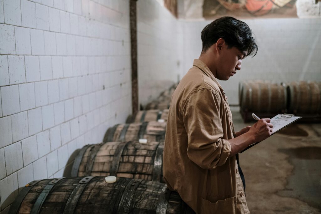 pexels-photo-5537791-5537791 A craft beer expert inspects wooden barrels in a brewery's storage room.